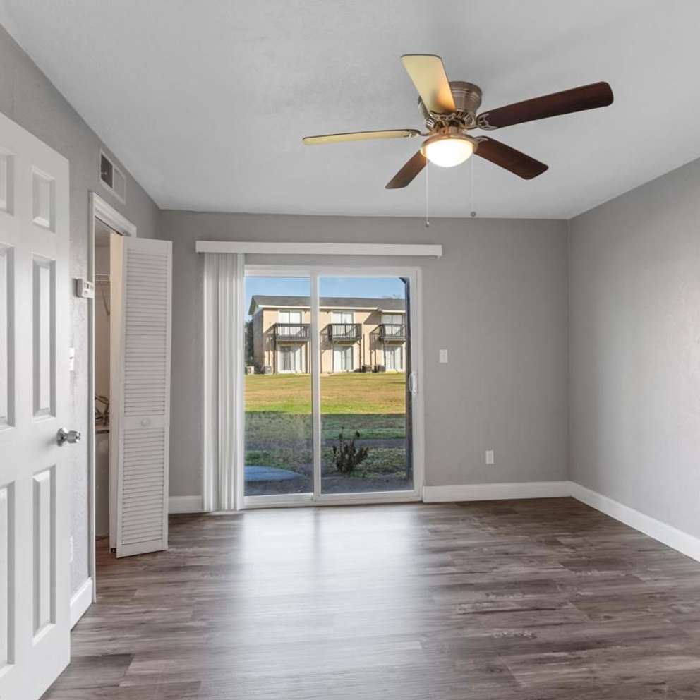 A room with a ceiling fan and sliding glass doors leading to a backyard.